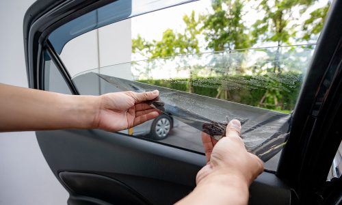 Car side window film removal and tinting installation. Male auto specialist worker hand gently carefully peeling off the old protective car film from glass surface.